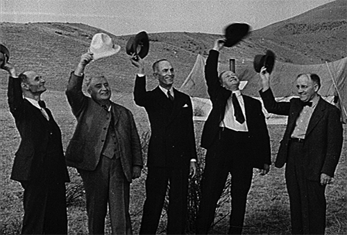 Film still showing 5 men in suits taking their hats off in b/w.